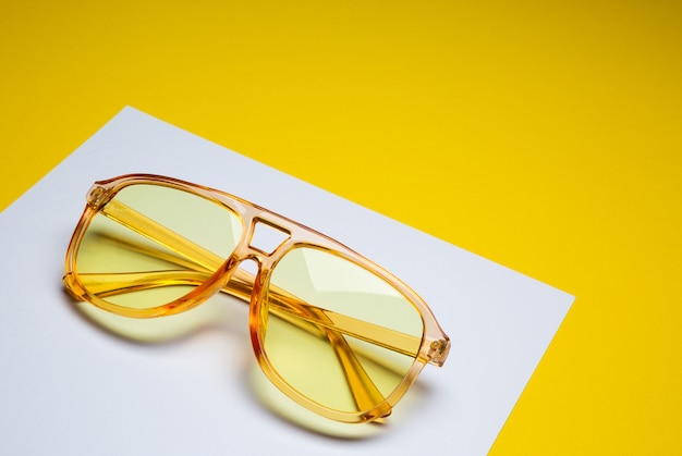 Óculos de sol amarelos femininos elegantes isolados no abstrato de papel branco e amarelo com espaço para texto
