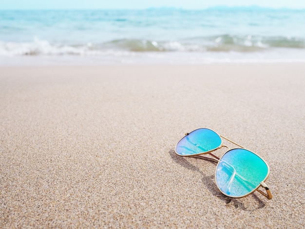 Óculos de sol com lente azul na areia na praia do sol.