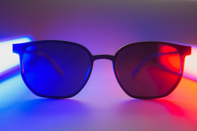 Óculos de sol elegantes filmados usando iluminação colorida abstrata rosa e azul com espaço de cópia.