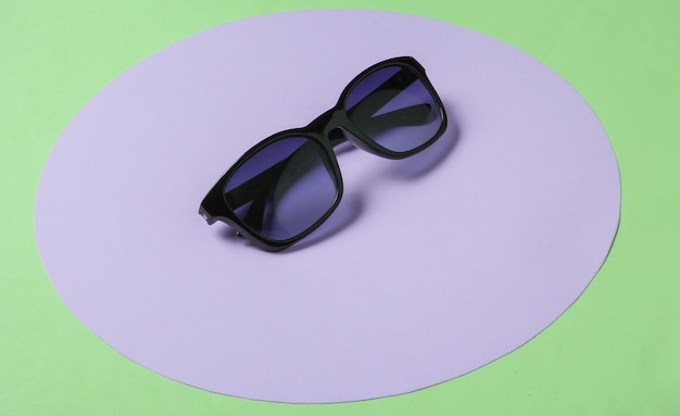 Óculos de sol sobre fundo verde com círculo roxo pastel. Conceito de moda minimalista