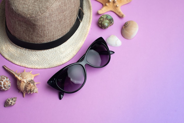 Óculos de verão acessórios, conchas, chapéu e sol no fundo rosa. Férias de verão e conceito de mar.