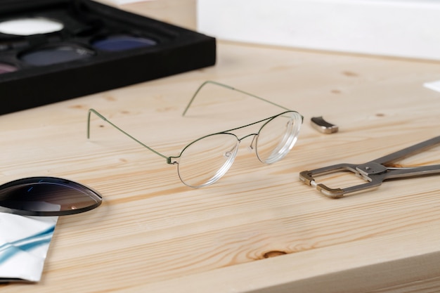 Óculos e alicates especiais para consertar armações de óculos colocados em mesa em oficina de ótica