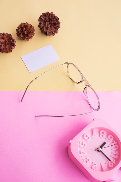 Óculos elegantes sobre fundo pastel. Cartão De Visita, Rosa Pastel E Cores Amarelas. Despertador, flores de árvore de abeto.