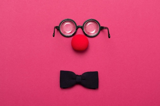 Óculos engraçados, nariz de palhaço vermelho e gravata estão sobre um fundo colorido como um rosto