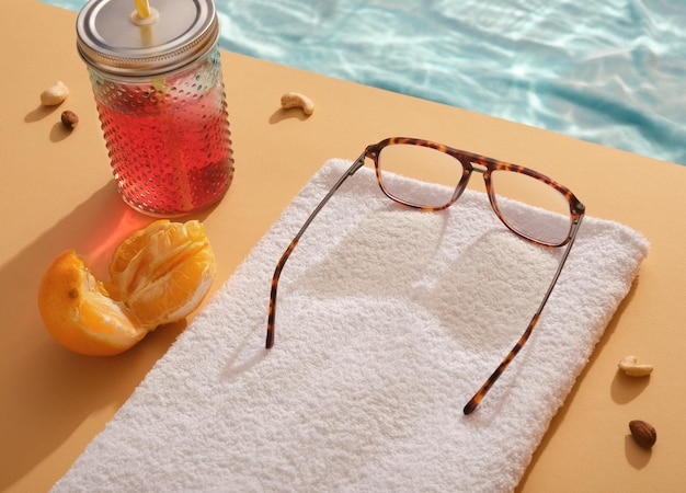 Óculos estão na toalha branca com vista para o mar tropical transparente cintilante. Coquetel revigorante, laranja suculenta fatiada, nozes espalhadas. A ideia ensolarada da praia de verão relaxa.