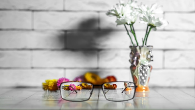 Óculos para visão com dioptrias em uma moldura preta em um fundo de flores e uma parede de tijolos