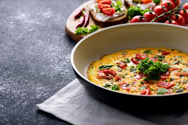 Cultivo de huevos revueltos con tomates, espinacas y semillas de calabaza en una sartén con tostadas con requesón, salsa pesto, chile y tomates cherry sobre fondo negro