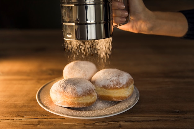 Foto cultivo a mano derramando azúcar en polvo en donas