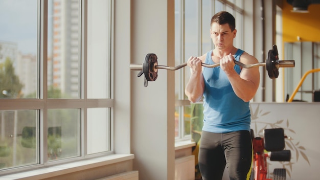 Culturismo en el gimnasio - hombre musculoso entrenando sus bíceps cerca del espejo, cerrar