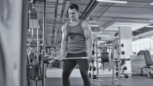 Culturismo en el gimnasio - hombre musculoso realizar ejercicios con barra de bíceps, blanco y negro - vista cercana