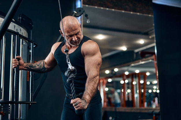 Culturista adulto hombre calvo haciendo ejercicio de peso pesado para tríceps mientras está en el concepto de culturismo de gimnasio