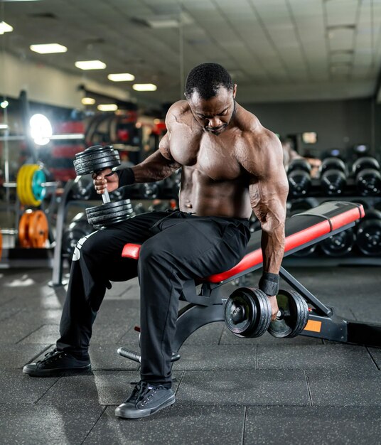 Culturista afroamericano sin camisa haciendo ejercicio para las manos Abdominales fuertes Fondo de gimnasio oscuro Vista completa