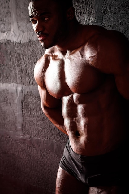 El culturista se apoya en la pared Atleta masculino afroamericano posando demostrando desarrollo muscular