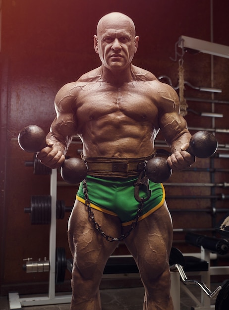 Culturista de atleta de moda antigua haciendo ejercicios de brazo en el gimnasio. Brutal estilo deportivo calvo caucásico de los años 80. Concepto de deporte, fitness y entrenamiento de los 80