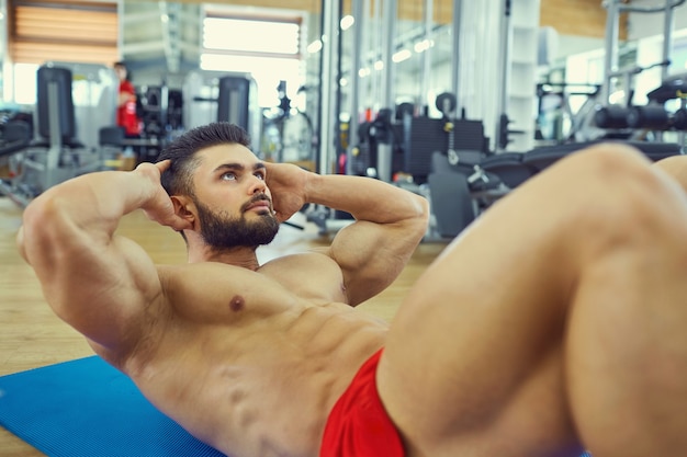 Culturista con barba hace ejercicios de abdominales en el suelo del gimnasio.