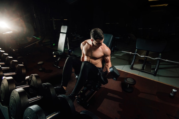 Culturista de chico atlético muy poderoso, ejecutar ejercicio con pesas, en el gimnasio oscuro