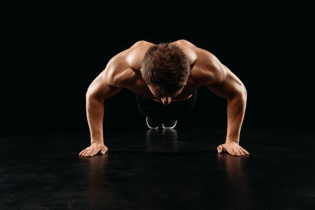 Culturista deportivo muscular haciendo flexiones aislado en negro