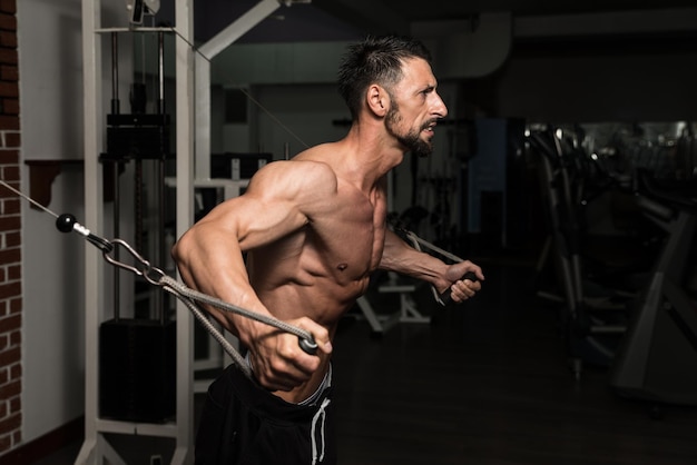 El culturista está trabajando en su pecho con un cruce de cables en un gimnasio oscuro