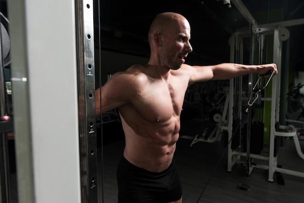 Culturista de fitness muscular haciendo ejercicio de peso pesado para hombros en máquina de cable en el gimnasio