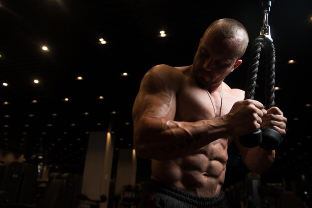 Culturista de fitness muscular haciendo ejercicio de peso pesado para tríceps en la máquina en el gimnasio