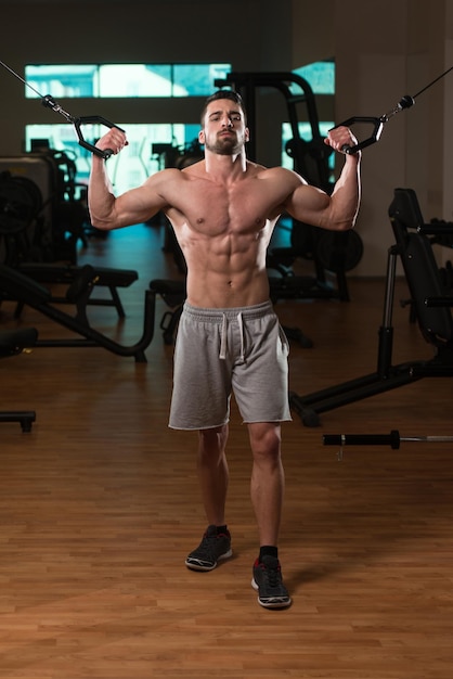 Culturista de fitness muscular joven haciendo ejercicio de peso pesado para bíceps en máquina con cable en el gimnasio