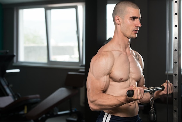 Culturista de fitness muscular joven haciendo ejercicio de peso pesado para bíceps en máquina con cable en el gimnasio