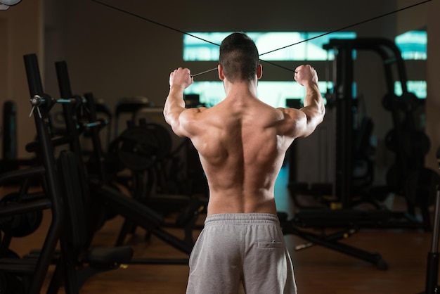 Culturista de fitness muscular joven haciendo ejercicio de peso pesado para la espalda o los hombros en la máquina en el gimnasio