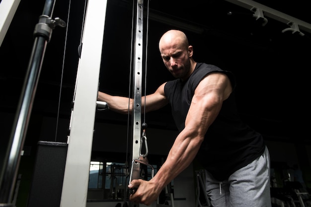 Culturista de fitness muscular joven haciendo ejercicio de peso pesado para tríceps en la máquina en el gimnasio