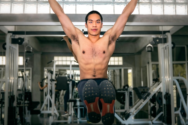 Culturista fuerte atlético hombre asiático entrenamiento ejercicio muscular abdominal (l-sit) en la barra de gimnasio.