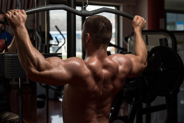 Culturista haciendo ejercicio de peso pesado para la espalda en la máquina en el gimnasio