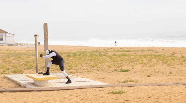 Un culturista haciendo ejercicios en la playa, usando audífonos. Concepto de deporte al aire libre.