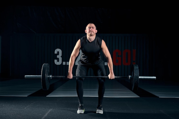 Culturista de hombre musculoso entrenando en gimnasio y posando. Ajuste el entrenamiento de tipo muscular con pesas y barra