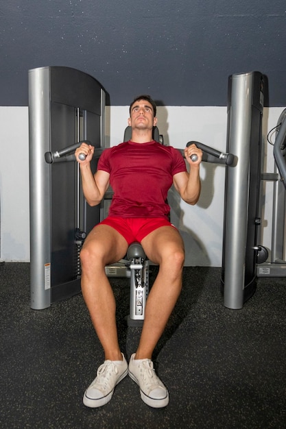 Culturista joven entrenando el hombro en la máquina de prensa