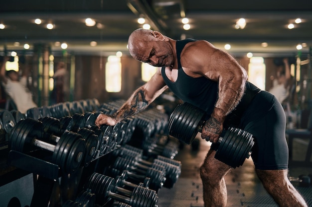 Culturista masculino adulto haciendo ejercicios con pesas mientras posa en el concepto de gimnasio de culturismo