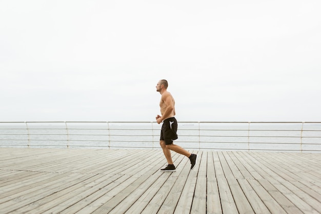 Culturista masculino musculoso se ejecuta en la playa. Concepto de estilo de vida saludable