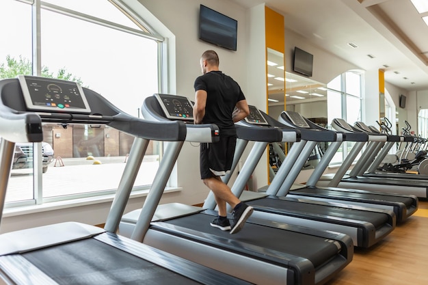 Culturista masculino musculoso guapo está haciendo ejercicio en una cinta en un gimnasio moderno. Entrenamiento cardiovascular