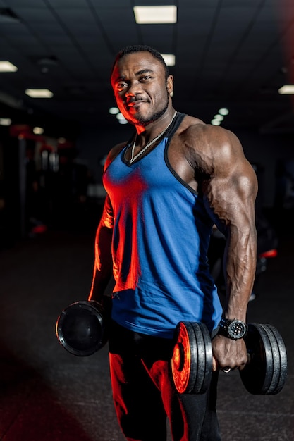 Culturista masculino trabajando con una pesa pesada. Fondo de gimnasio moderno. Camisa azul.