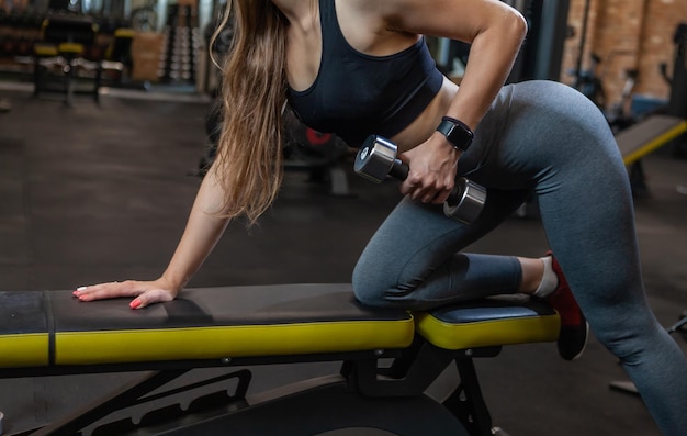 Culturista de mujer de belleza en el gimnasio levantando pesas en un banco en el gimnasio moderno