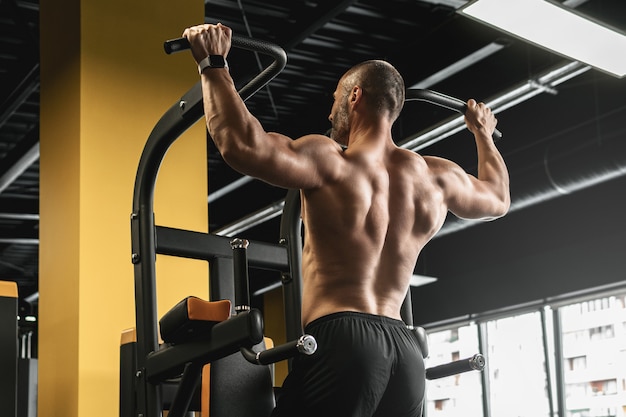 Culturista muscular haciendo dominadas durante su entrenamiento en el gimnasio