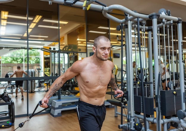 Culturista musculoso con ejercicios de torso desnudo en máquina de cruce de cable. Hombres fitness bombeo de los músculos en el gimnasio.