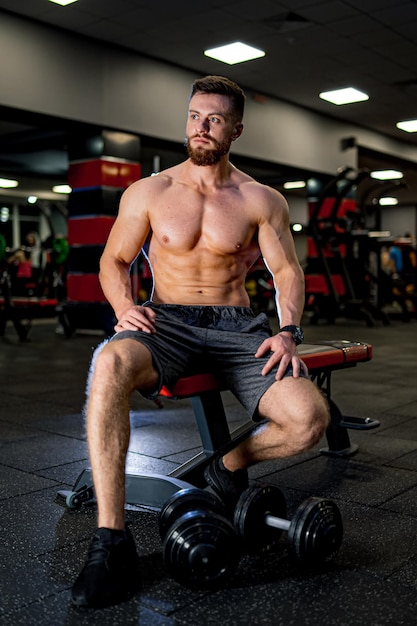 Un culturista musculoso guapo descansa después del entrenamiento. Hombre fuerte sin camisa descansando después de un entrenamiento activo.