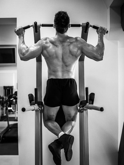 Un culturista musculoso haciendo pulling up en la barra en un gimnasio moderno