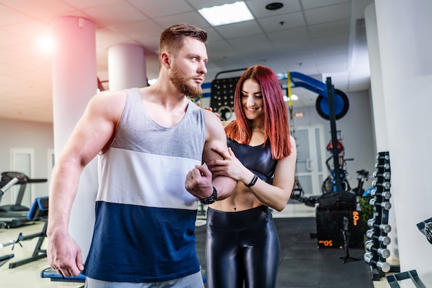 Culturista musculoso muestra sus bíceps a la joven y bella mujer en el centro deportivo. mujer sorprendida tocando el brazo del hombre mientras está de pie cerca del atleta en el gimnasio de crossfit.