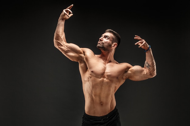 Culturista posando. Hombre musculoso fitness en pared oscura.