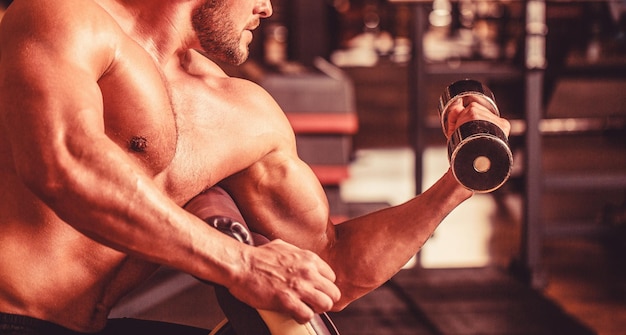 Culturista trabajando con pesas con mancuernas en el gimnasio Hombre levantando mancuernas en un gimnasio haciendo ejercicio para los músculos Hombre culturista haciendo ejercicios con mancuernas