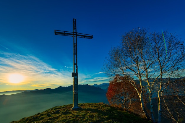 Cumbre de una montaña con cruz antes del atardecer con colores otoñales