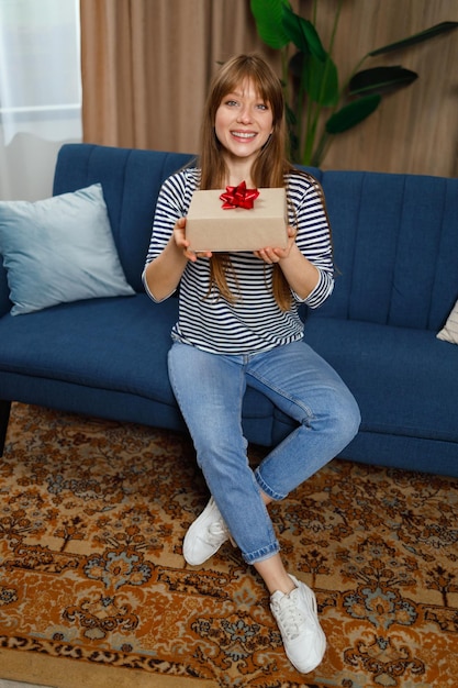 La cumpleañera está sentada en casa en el sofá con una caja de regalo