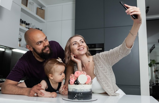 Foto cumpleaños feliz concepto de familia mamá joven toma un selfie de su hija y esposo con un pastel en la cocina