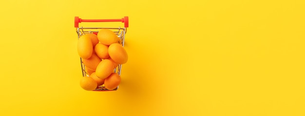 Cumquat ou kumquat em um carrinho de compras em fundo amarelo