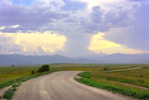 Cúmulos espesos en la noche sobre una llanura montañosa con un camino rural. Siberia, Rusia